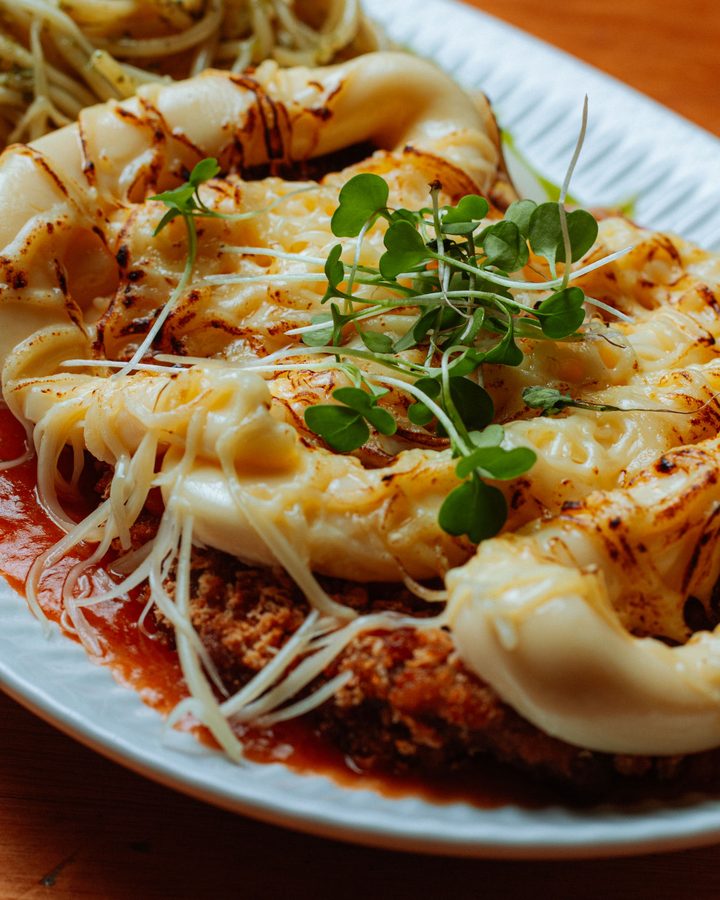 Parmegiana coberta de queijo gratinado e brotos, com espaguete ao lado