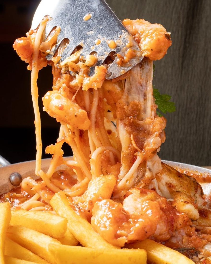 Pegador levantando o camarão à parmegiana, com o espaguete e a mussarela puxando sobre as fritas